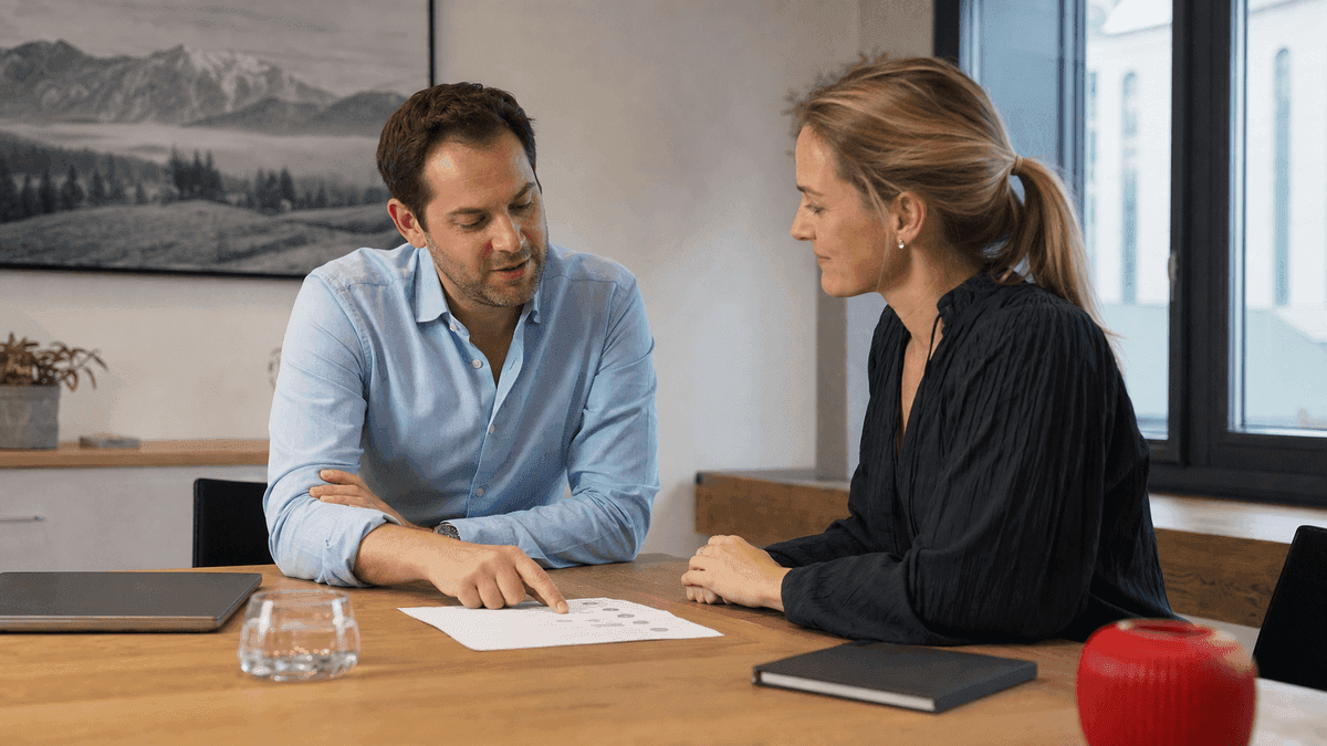 A web consultant and a client in a friendly advisory meeting at a clean Austrian office, one pointing at a printed checklist on the table while the other listens, warm natural light, authentic candid business moment, photorealistic, no readable text